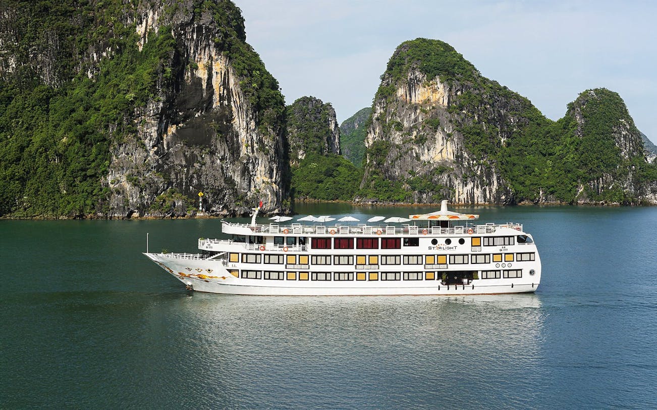 Starlight Cruise sailing in Halong Bay with limestone cliffs in the background.