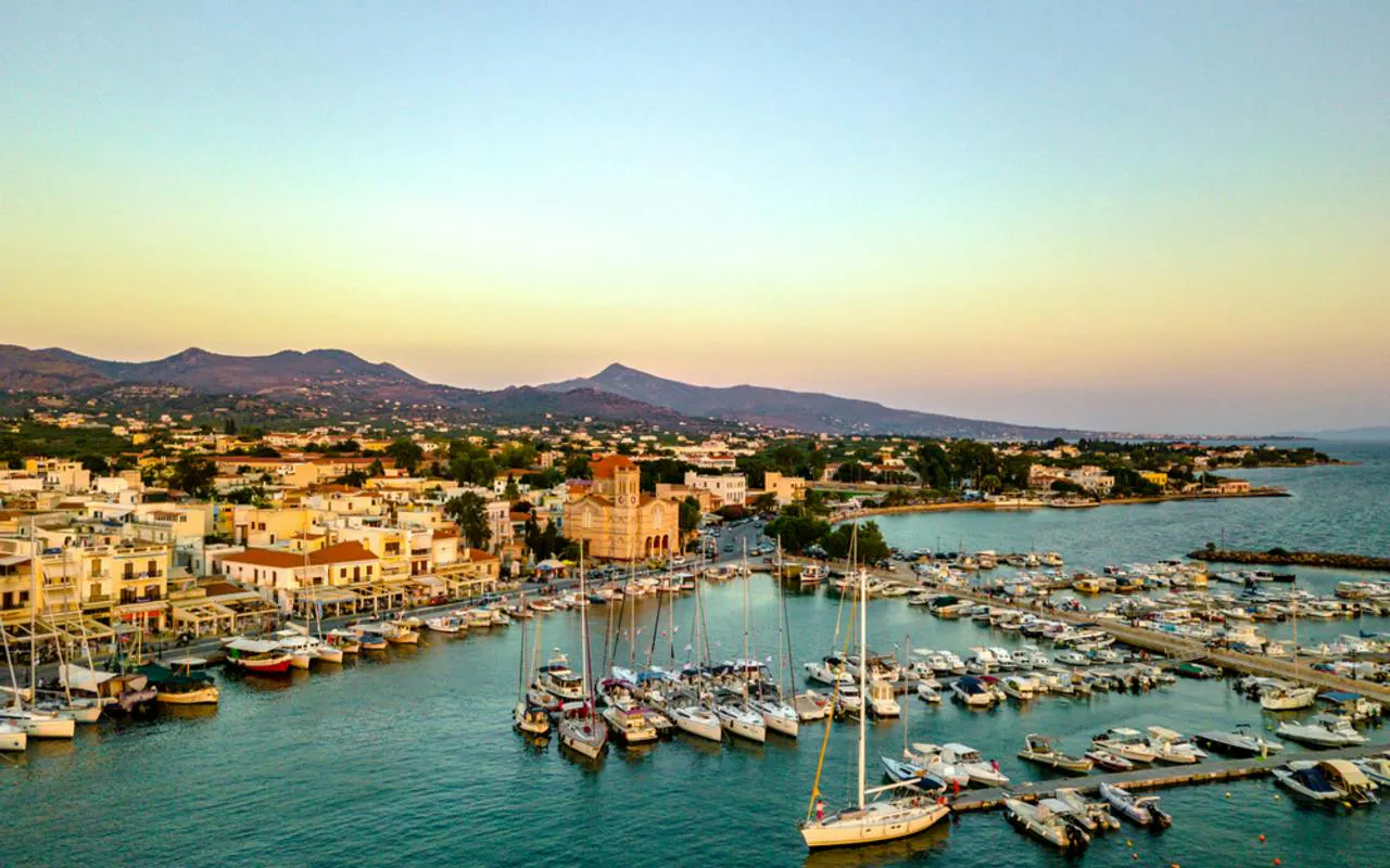Boats docked at Aegina harbor with mountains in the background, Greece.