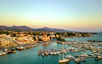 Boats docked at Aegina harbor with mountains in the background, Greece.