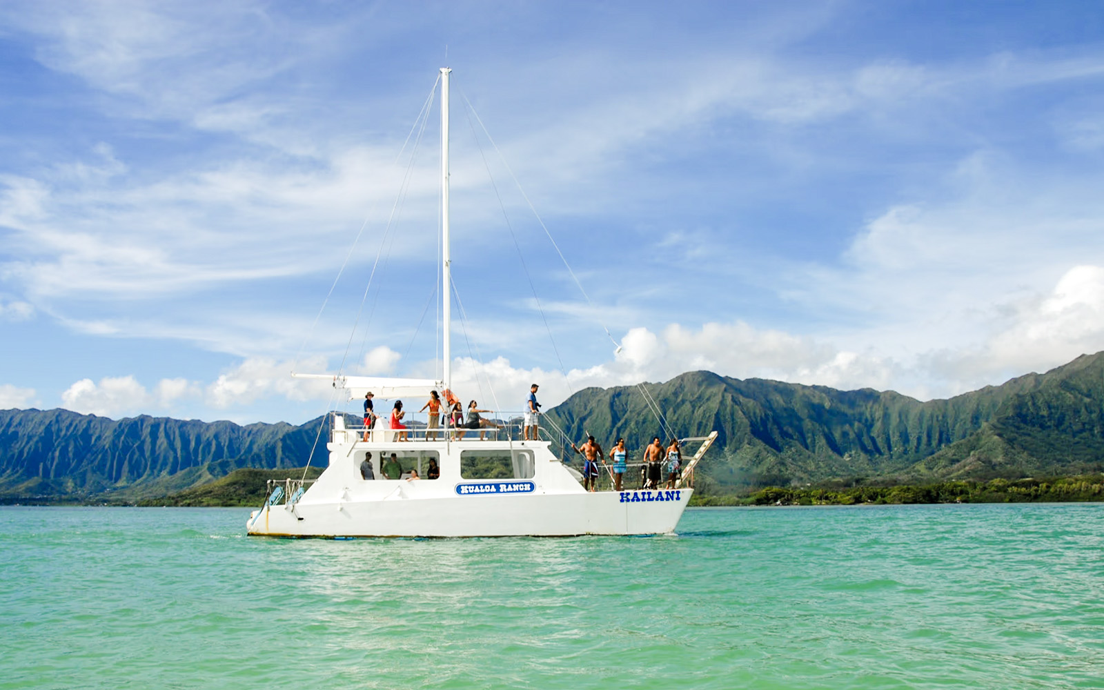 Boat tour on turquoise waters with mountains in background, Kualoa Ranch, Hawaii.