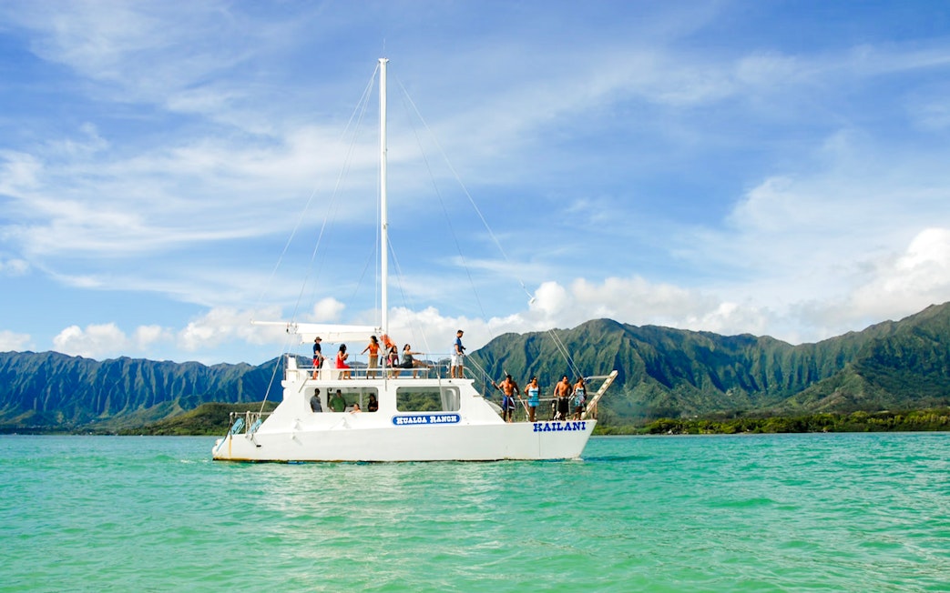 Boat tour on turquoise waters with mountains in background, Kualoa Ranch, Hawaii.