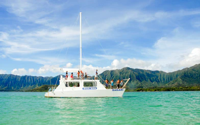 Boat tour on turquoise waters with mountains in background, Kualoa Ranch, Hawaii.