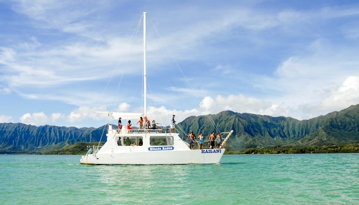 Boat tour on turquoise waters with mountains in background, Kualoa Ranch, Hawaii.