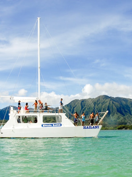 Boat tour on turquoise waters with mountains in background, Kualoa Ranch, Hawaii.