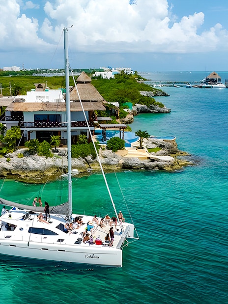 Catamaran sailing near Isla Mujeres with a coastal resort in view.