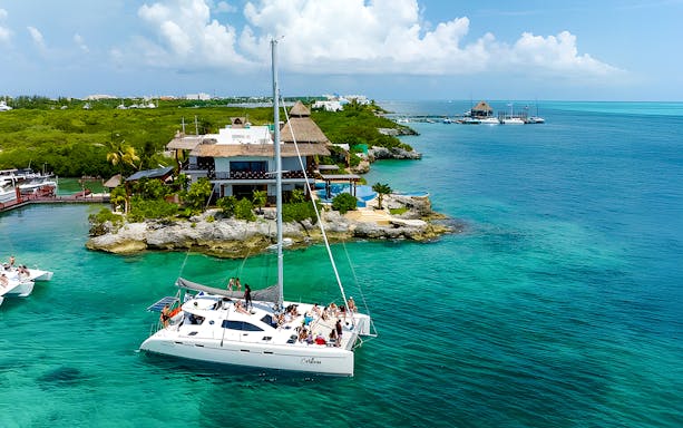 Catamaran sailing near Isla Mujeres with a coastal resort in view.