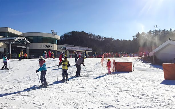 Skiers at Jisan Forest Ski Resort near J-Park building on a sunny day.