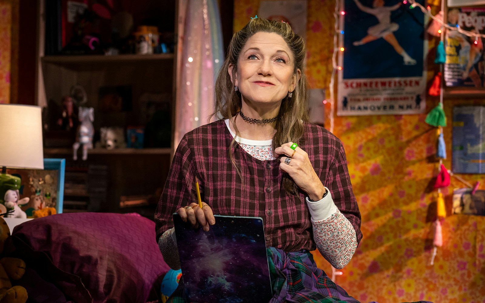 Person in a cozy room holding a pencil and notebook, related to Kimberly Akimbo.