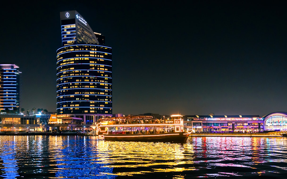 Dubai cruise boat illuminated on Dubai Water Canal at night.