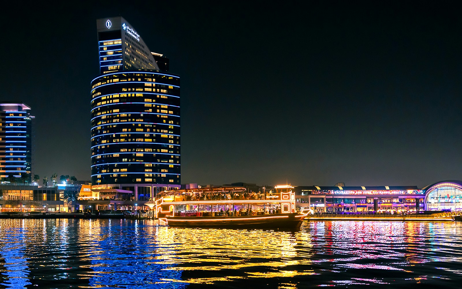 Dubai cruise boat illuminated on Dubai Water Canal at night.