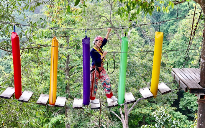 Woman crossing a colorful step bridge in a forest adventure park.