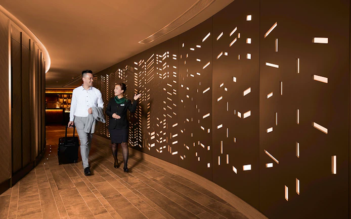 First-class lounge entrance at Hong Kong International Airport with a guest and staff member.