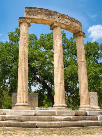 Ancient Olympia ruins with three standing columns in Greece.