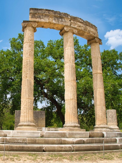 Ancient Olympia ruins with three standing columns in Greece.
