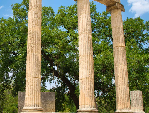 Ancient Olympia ruins with three standing columns in Greece.