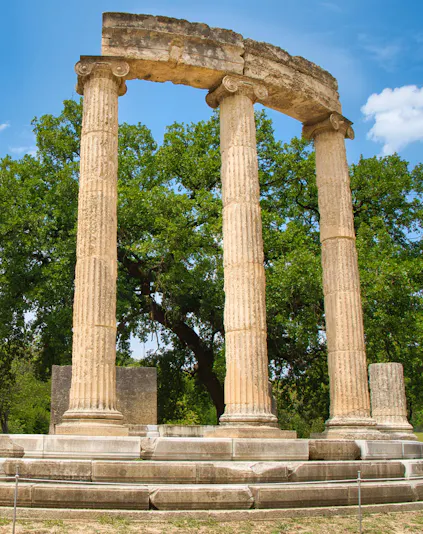 Ancient Olympia ruins with three standing columns in Greece.