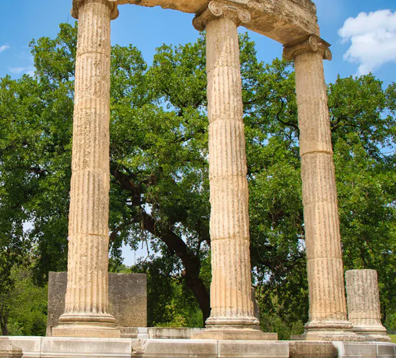Ancient Olympia ruins with three standing columns in Greece.