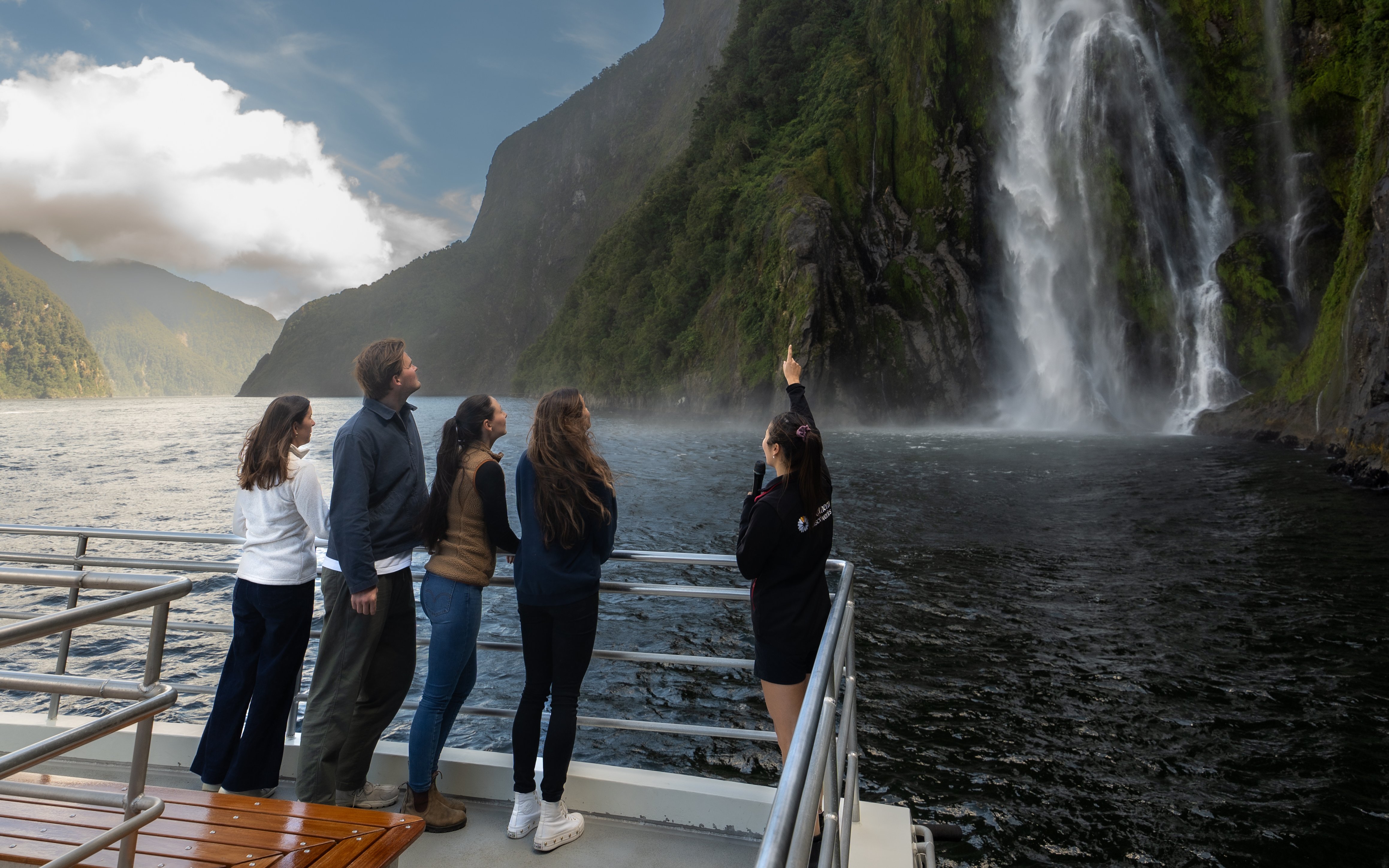 Tourists on a boat admire a waterfall at Milford Sound, New Zealand.