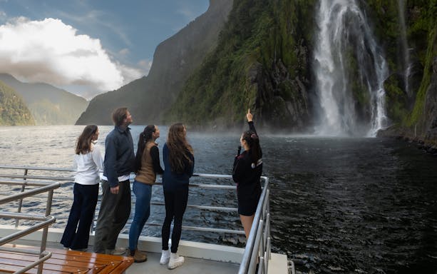 Tourists on a boat admire a waterfall at Milford Sound, New Zealand.