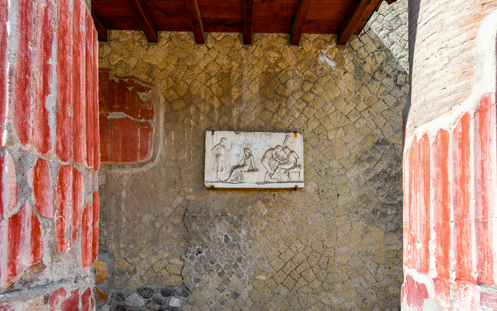 Ancient fresco in Herculaneum with red columns and stone wall, seen on a Sorrento tour.