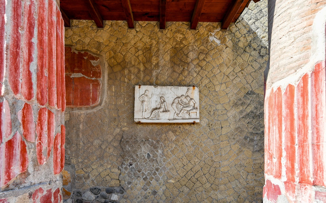 Ancient fresco in Herculaneum with red columns and stone wall, seen on a Sorrento tour.