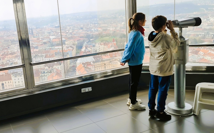 Children using a telescope inside Zizkov TV Tower with Prague city view.