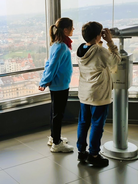Children using a telescope inside Zizkov TV Tower with Prague city view.