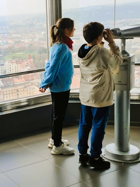 Children using a telescope inside Zizkov TV Tower with Prague city view.