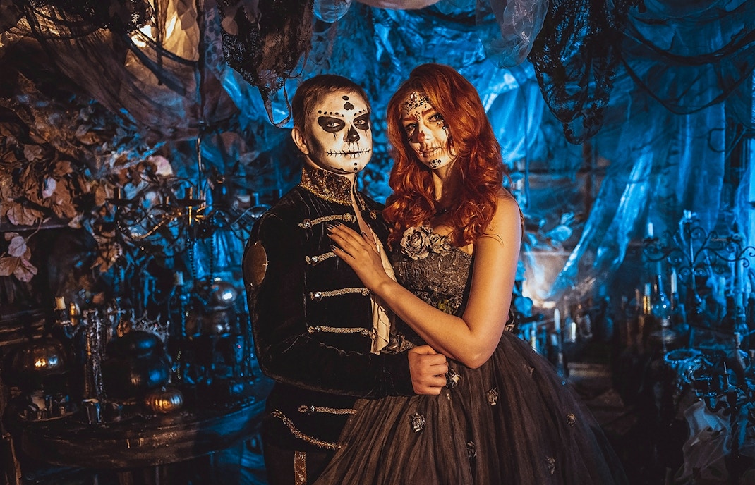 Couple in Halloween costumes with face paint in a Parisian-themed setting.