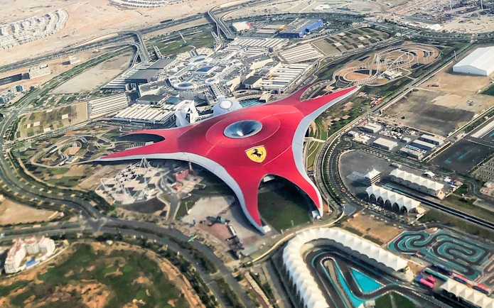 Aerial view of Ferrari World Abu Dhabi on Yas Island, featuring its iconic red roof and surrounding attractions.