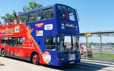 Liverpool hop on hop off bus at a riverside stop with passengers on board.