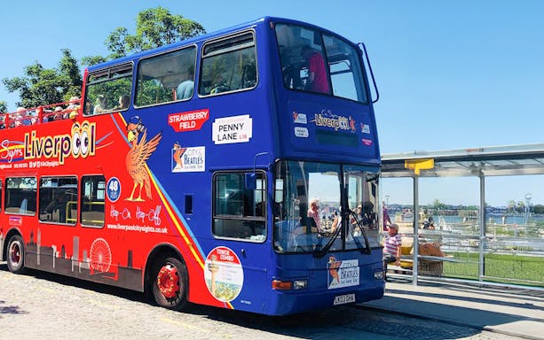 Liverpool hop on hop off bus at a riverside stop with passengers on board.