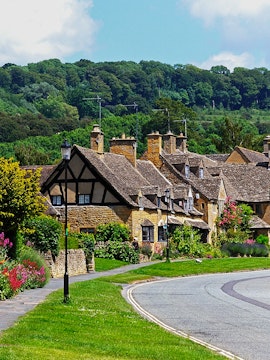 Cotswold village street with stone cottages and lush greenery, part of London to Cotswold tours.