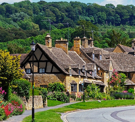 Cotswold village street with stone cottages and lush greenery, part of London to Cotswold tours.