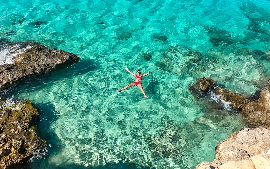Person floating in clear turquoise water near rocky shore, Gozo and Comino cruise.
