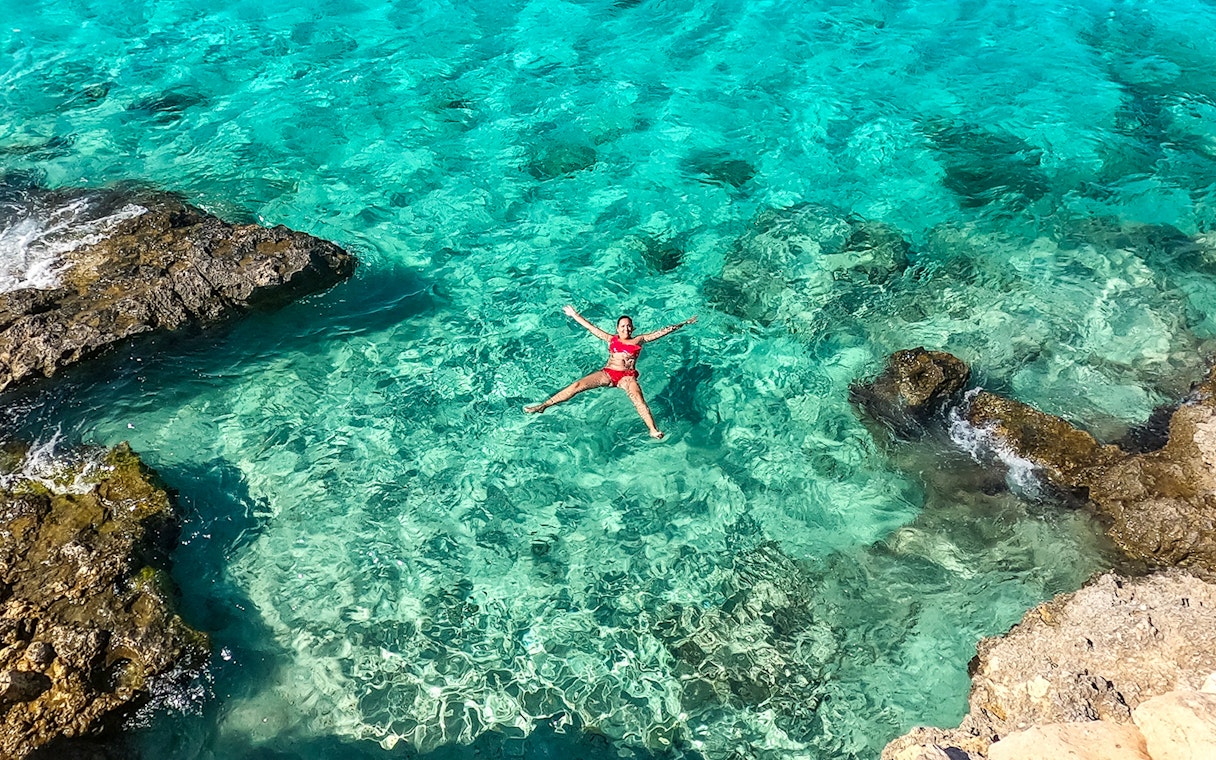 Person floating in clear turquoise water near rocky shore, Gozo and Comino cruise.