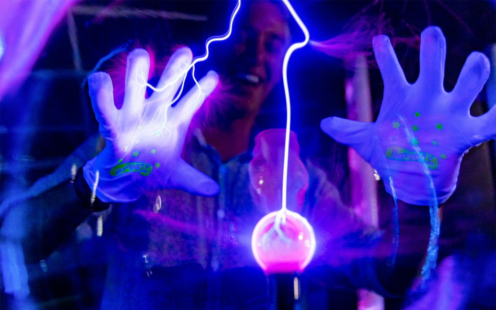 Hands interacting with glowing plasma ball at Infinity Attraction, Gold Coast.
