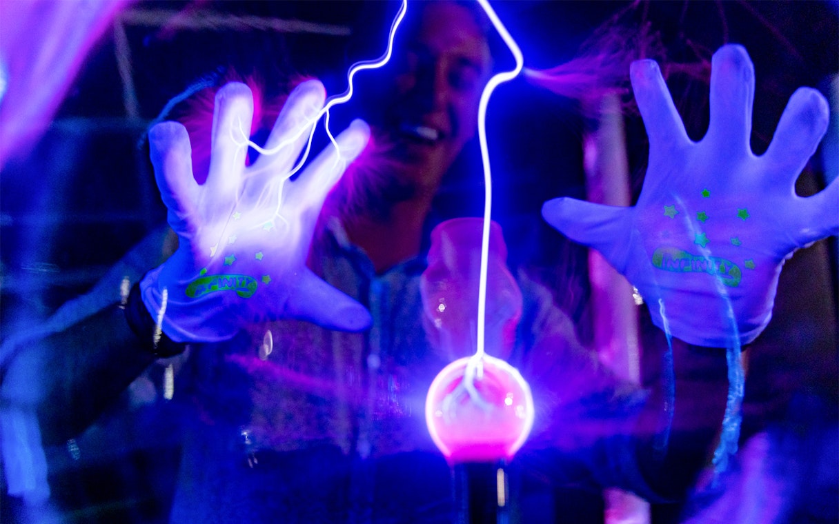 Hands interacting with glowing plasma ball at Infinity Attraction, Gold Coast.