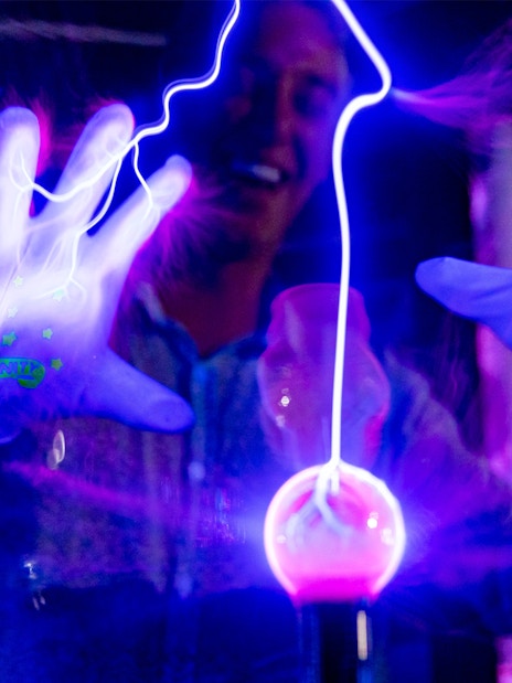 Hands interacting with glowing plasma ball at Infinity Attraction, Gold Coast.