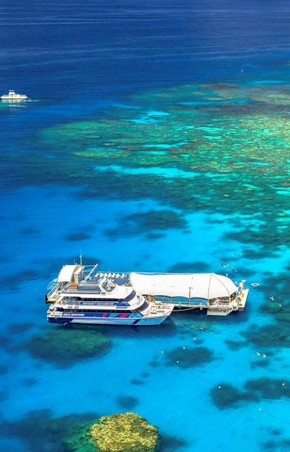 Cruise ship docked at Great Barrier Reef, Cairns, with vibrant coral visible underwater.