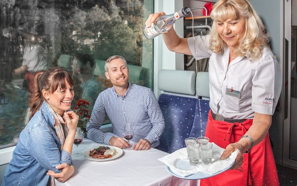 Travellers enjoying drinks on the Glacier Express with scenic views.