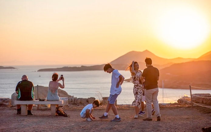 Guests watching sunset at Cape Sounion with sea and mountains in background.