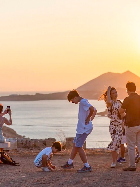 Guests watching sunset at Cape Sounion with sea and mountains in background.