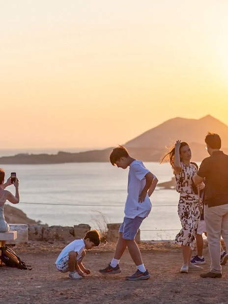 Guests watching sunset at Cape Sounion with sea and mountains in background.