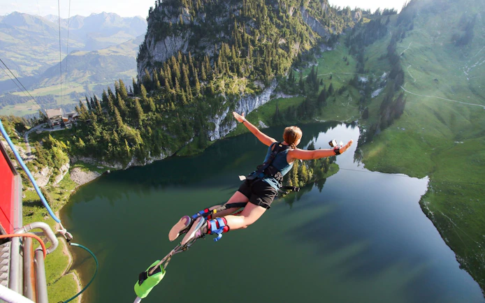 Person bungee jumping over Stockhorn Lake, Interlaken, surrounded by mountains.