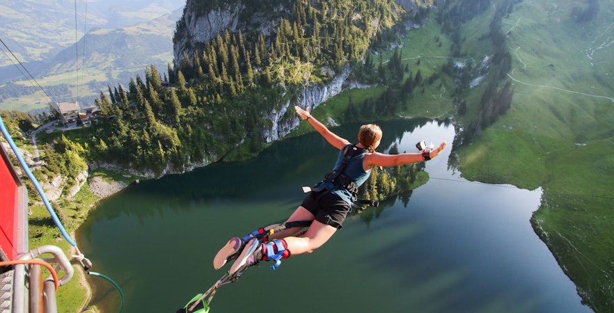 Person bungee jumping over Stockhorn Lake, Interlaken, surrounded by mountains.