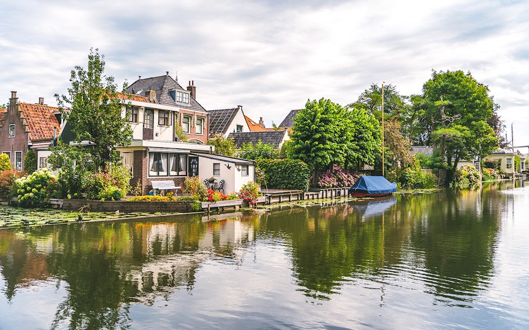Canal with houses and boat in Edam, Netherlands, surrounded by lush greenery.