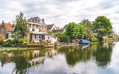 Canal with houses and boat in Edam, Netherlands, surrounded by lush greenery.