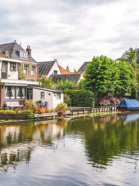 Canal with houses and boat in Edam, Netherlands, surrounded by lush greenery.
