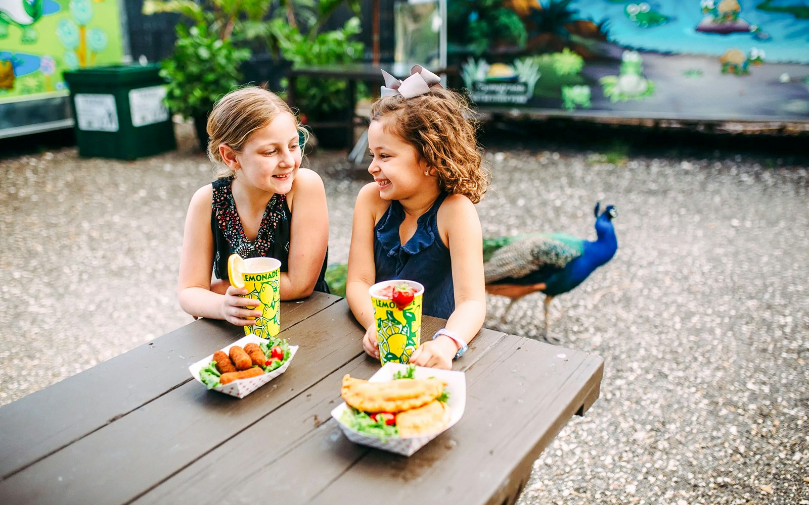 Kids enjoying a meal at Sawgrass Recreation Park with a peacock in the background.